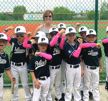 Baseball team posing for a photo wearing pink arm sleeves on a baseball field.
